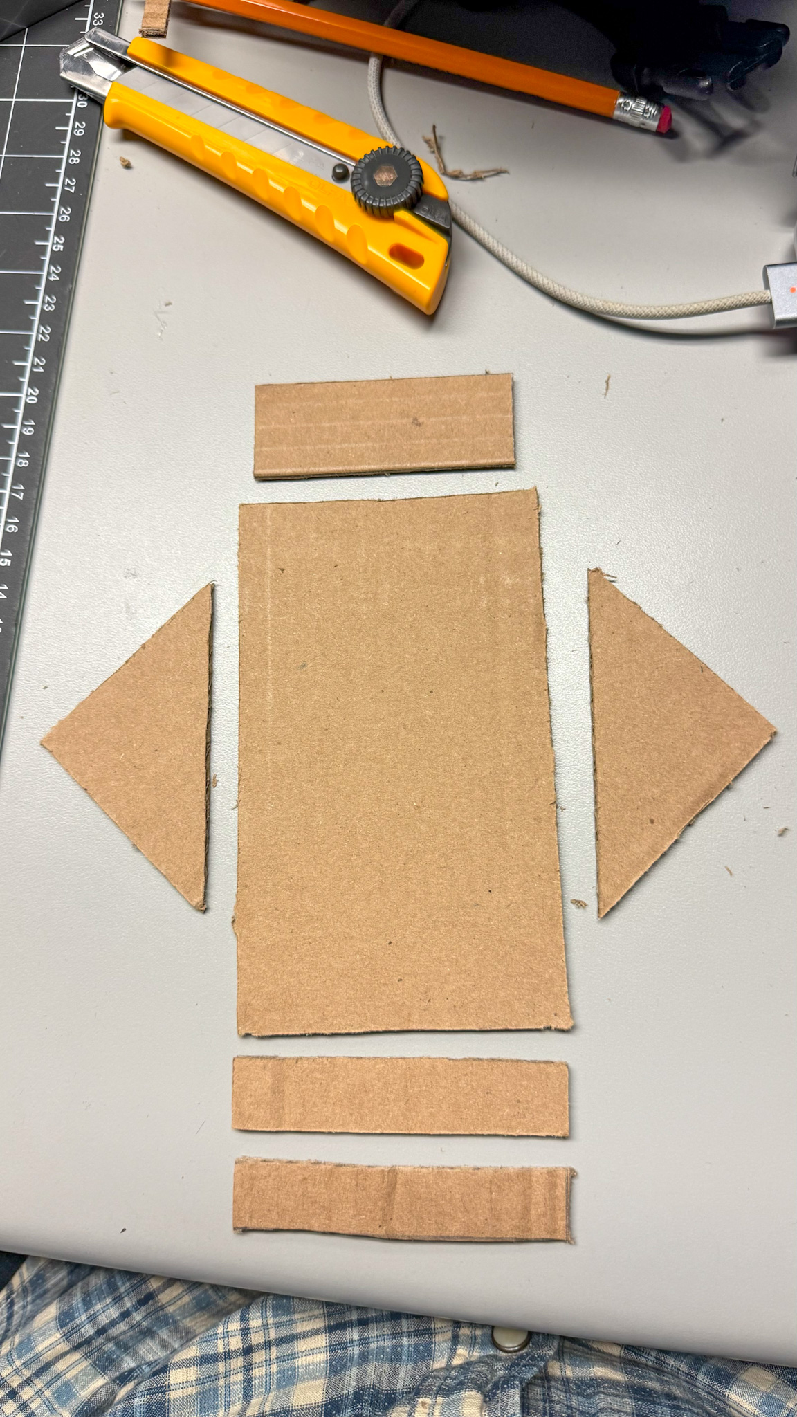 In this step, I began preparing my materials for the first prototype. I used cardboard as my primary material because it is lightweight, easy to cut, and ideal for quick experimentation. Using a utility knife, ruler, and pencil, I measured and cut several key pieces: one large rectangular base, two triangular supports, and three thin rectangular strips.
